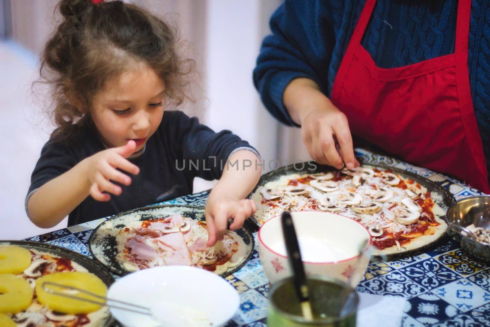 Young girl and mother making homemade pizzas in a domestic kitchen