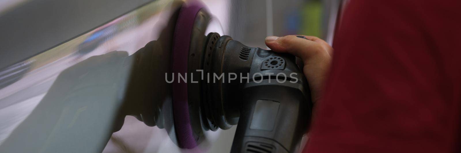 A repairman polishes a car body, close-up of a hand. Equipment for removing scratches, removing paint irregularities