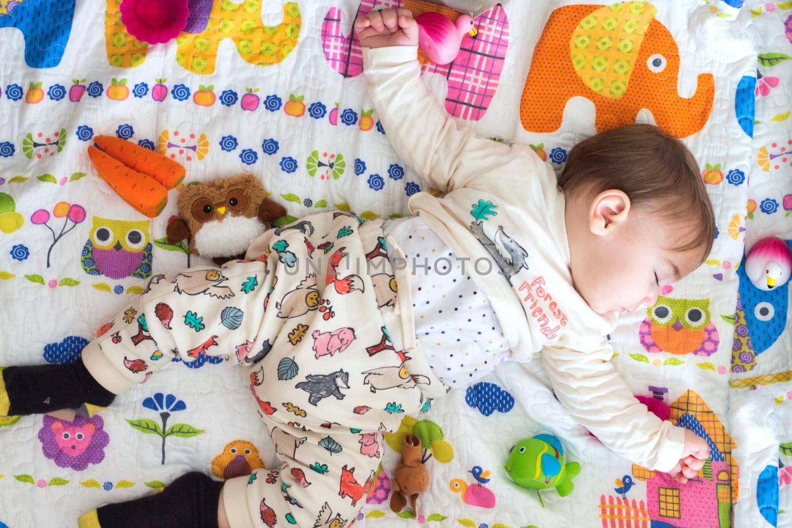 Adorable baby boy sleeping on a colorful mattress surrounded with toys