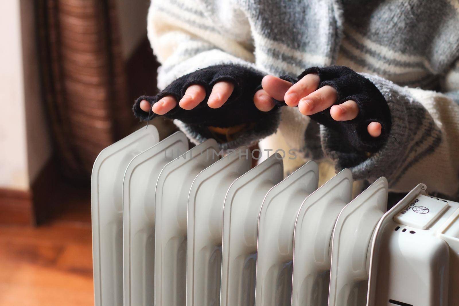 Person heating their hands at home over a domestic portable radiator in winter by tennesseewitney