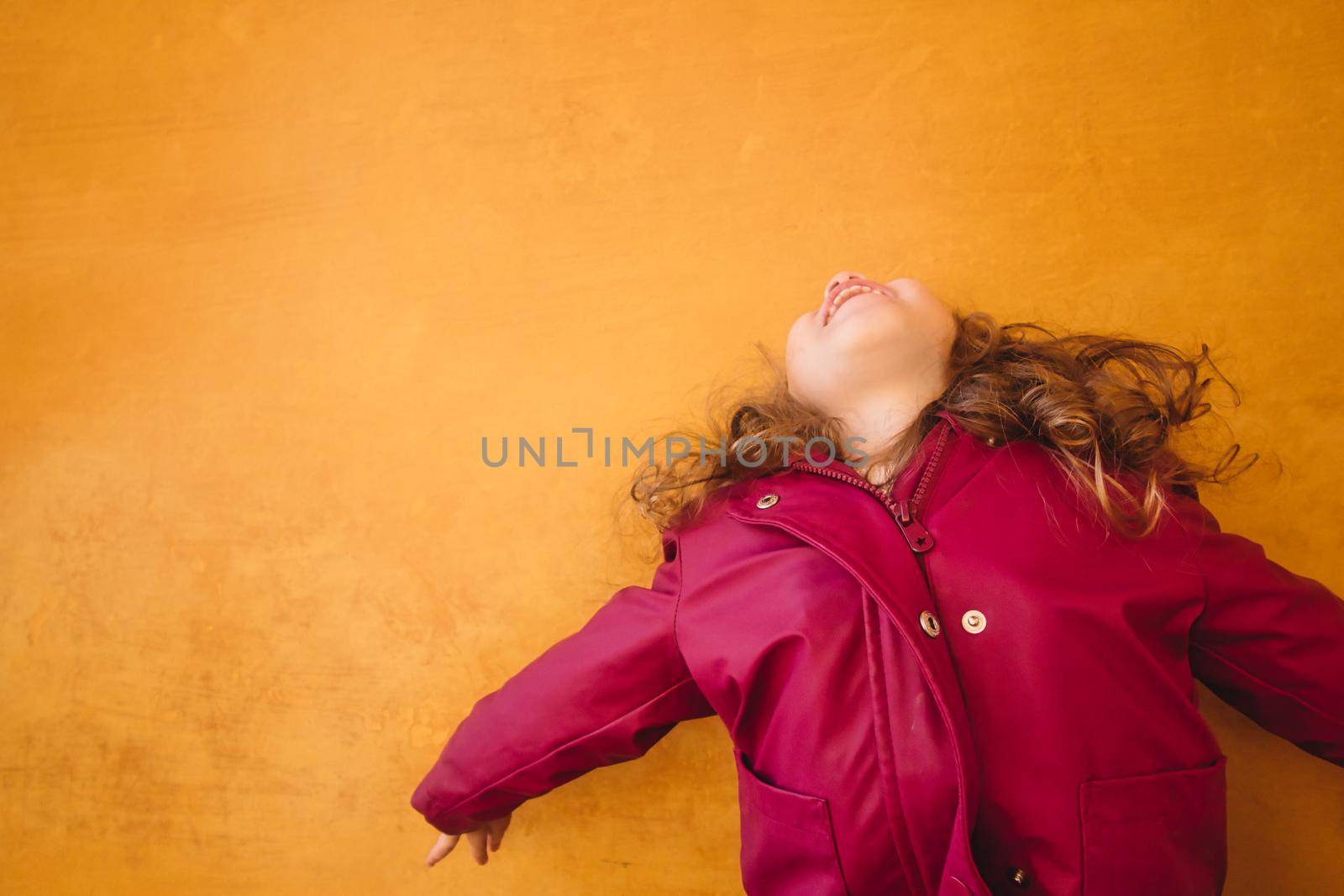Happy little girl jumping for joy against a colorful orange wall background