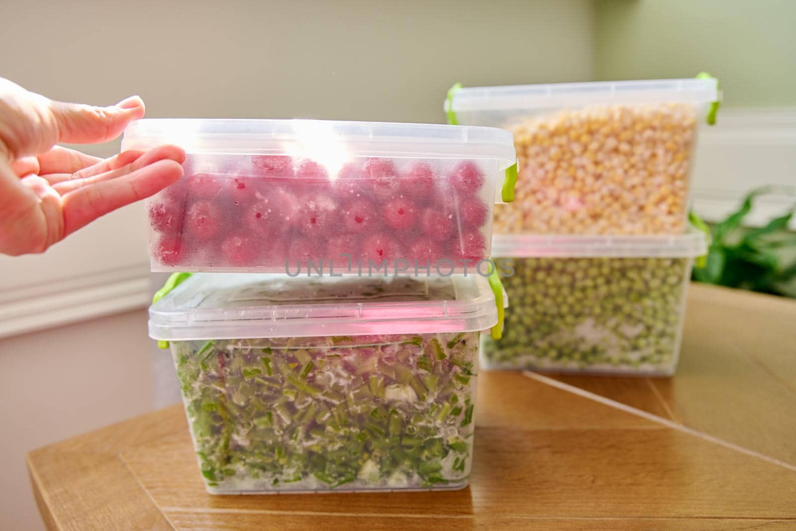 Frozen vegetables and fruits, close-up frozen in the freezer green onions, peas, cherry, corn in plastic containers. Seasonal vegetables, food preparations for the winter