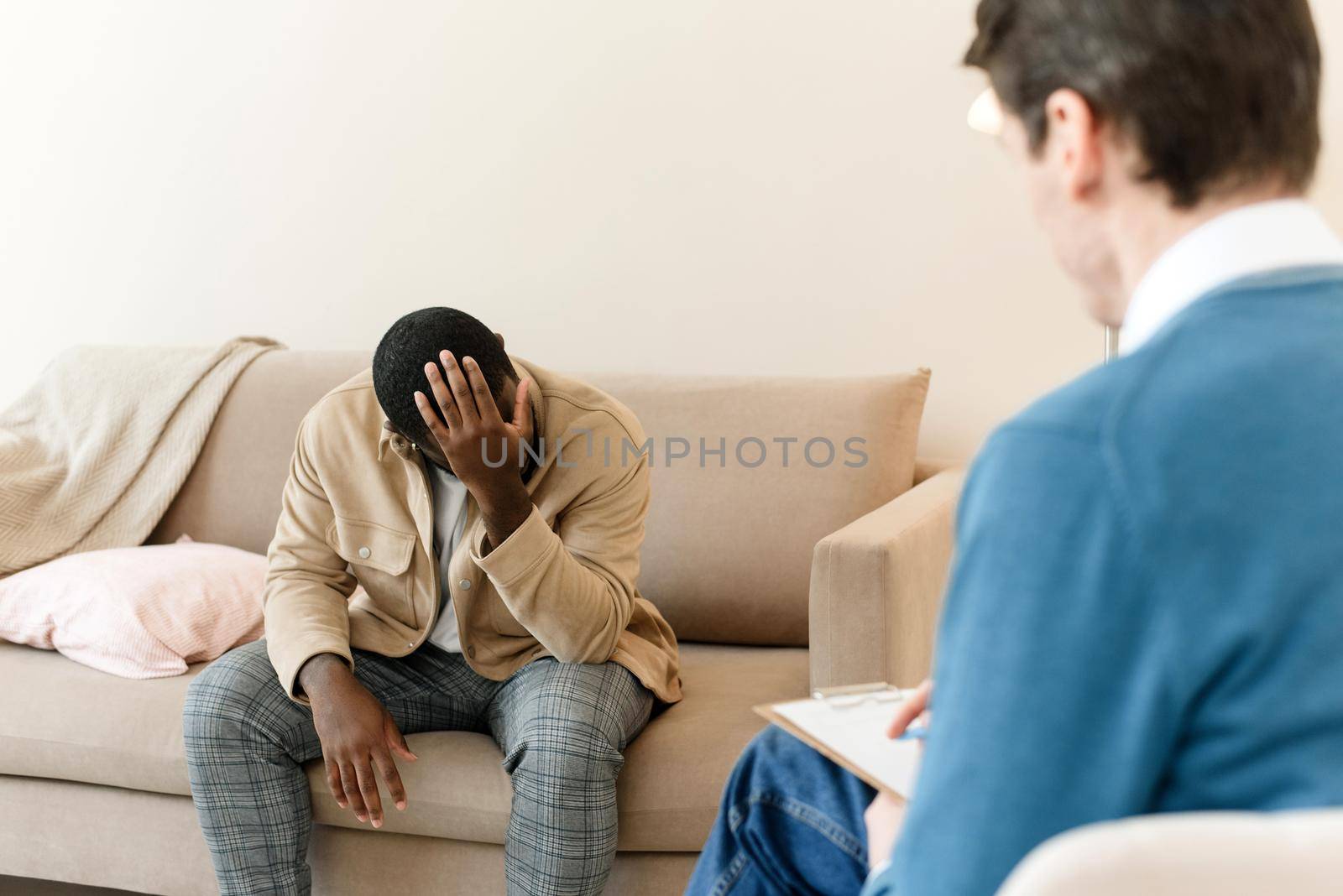 An irritated African American emotionally talks about problems to a psychologist at a session, a confused unhappy young man undergoes therapy with a psychiatrist