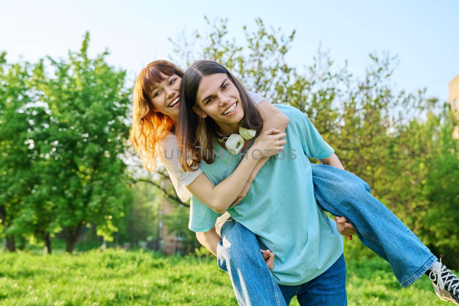 Couple of happy having fun teenagers together outdoor. Young teenage male and female laughing in park on lawn. Joy, happiness, friendship, summer, students, holidays, youth concept