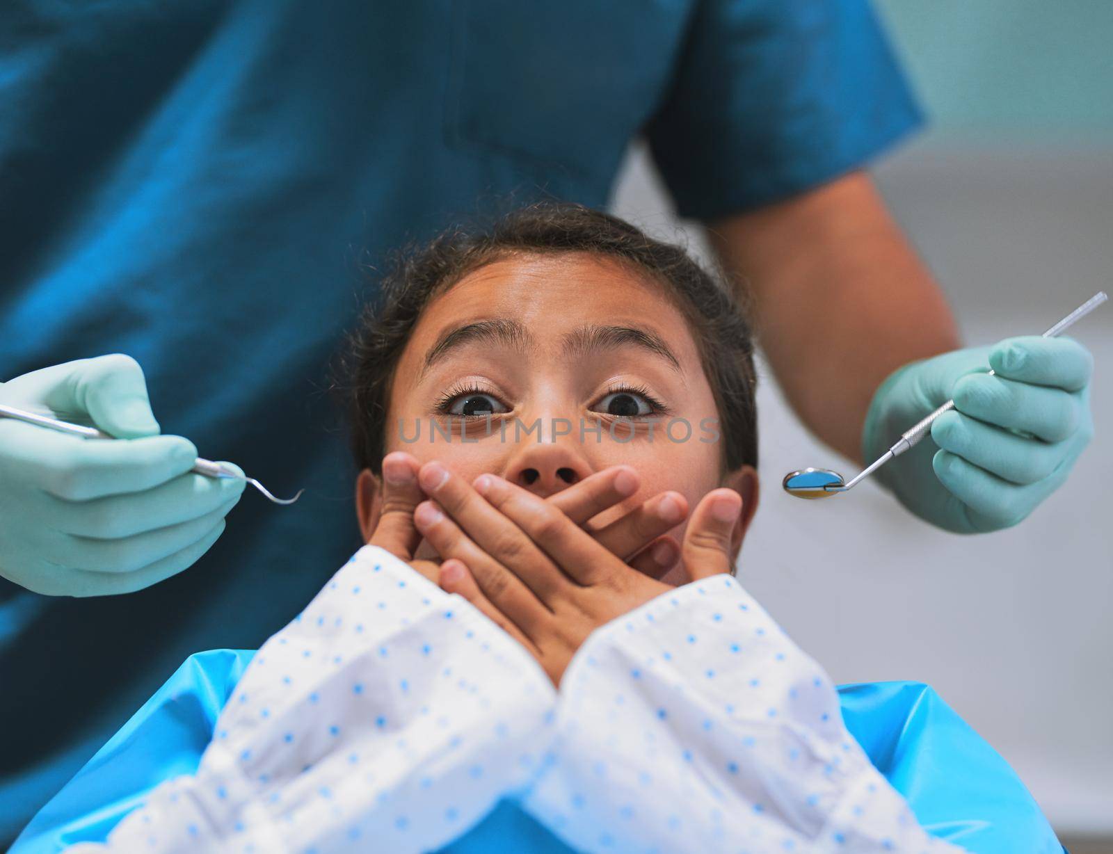 Shot of a frightened little girl lying down on a dentist chair and holds her mouth closed to keep the dentist from working on her.