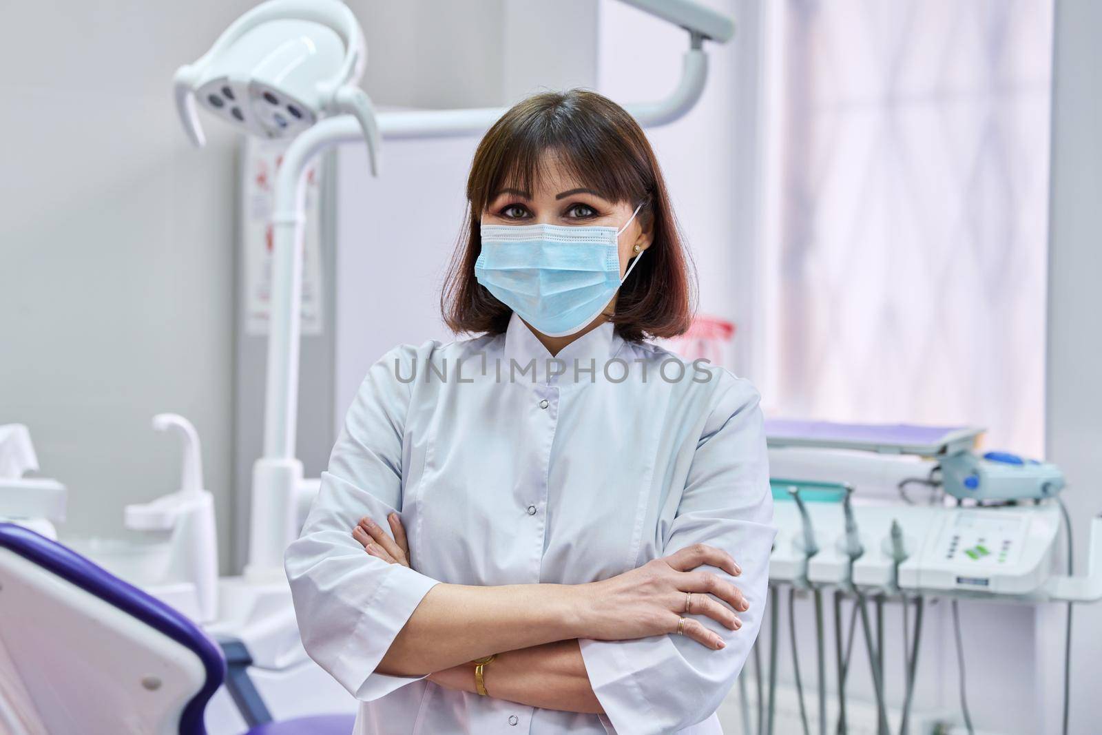 Portrait of confident female dentist doctor in office looking at camera. Middle aged female in medical protective mask. Dentistry, medicine, health care, profession, stomatology concept