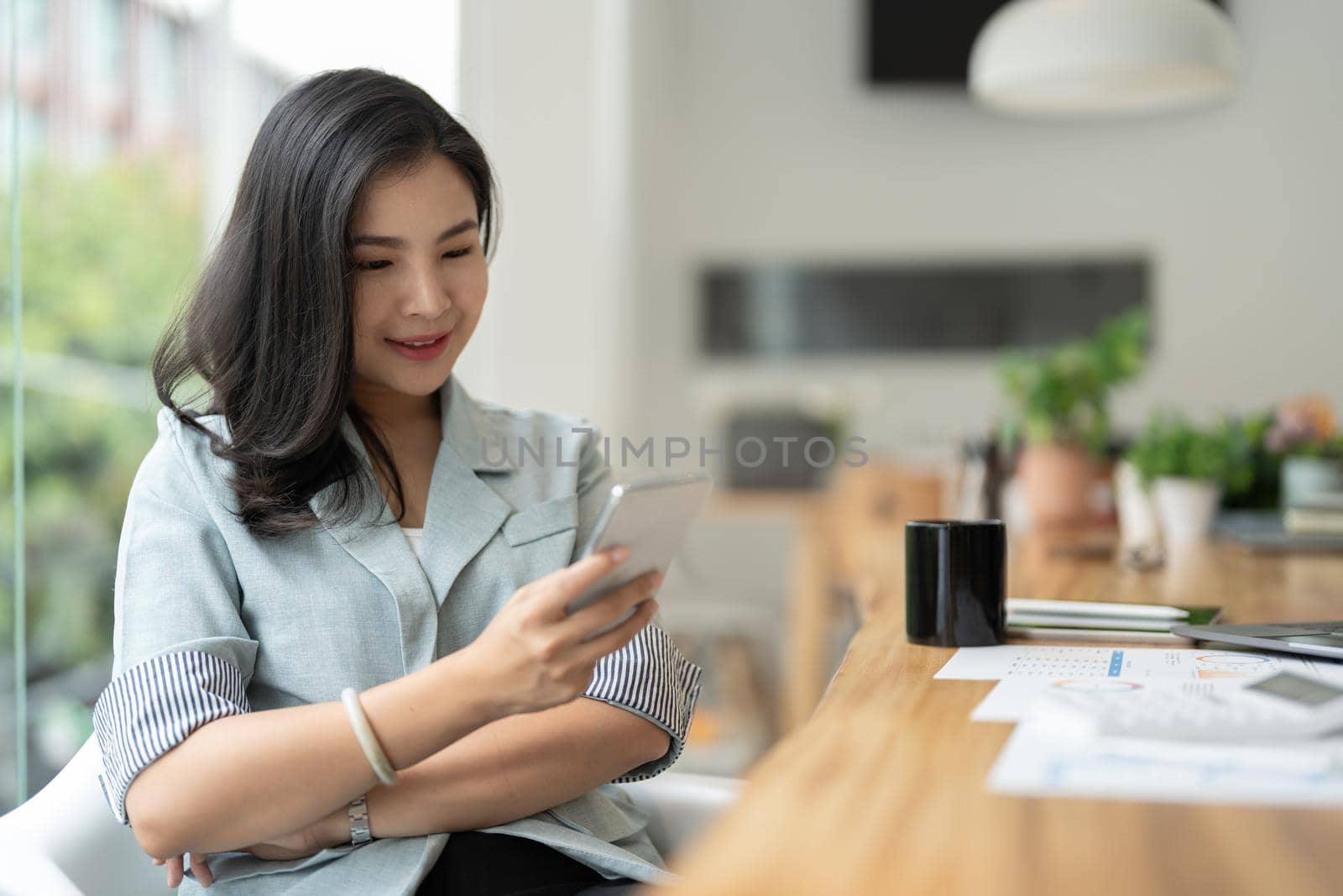 Smiling asian businesswoman using phone in office. Small business entrepreneur looking at her mobile phone and smiling