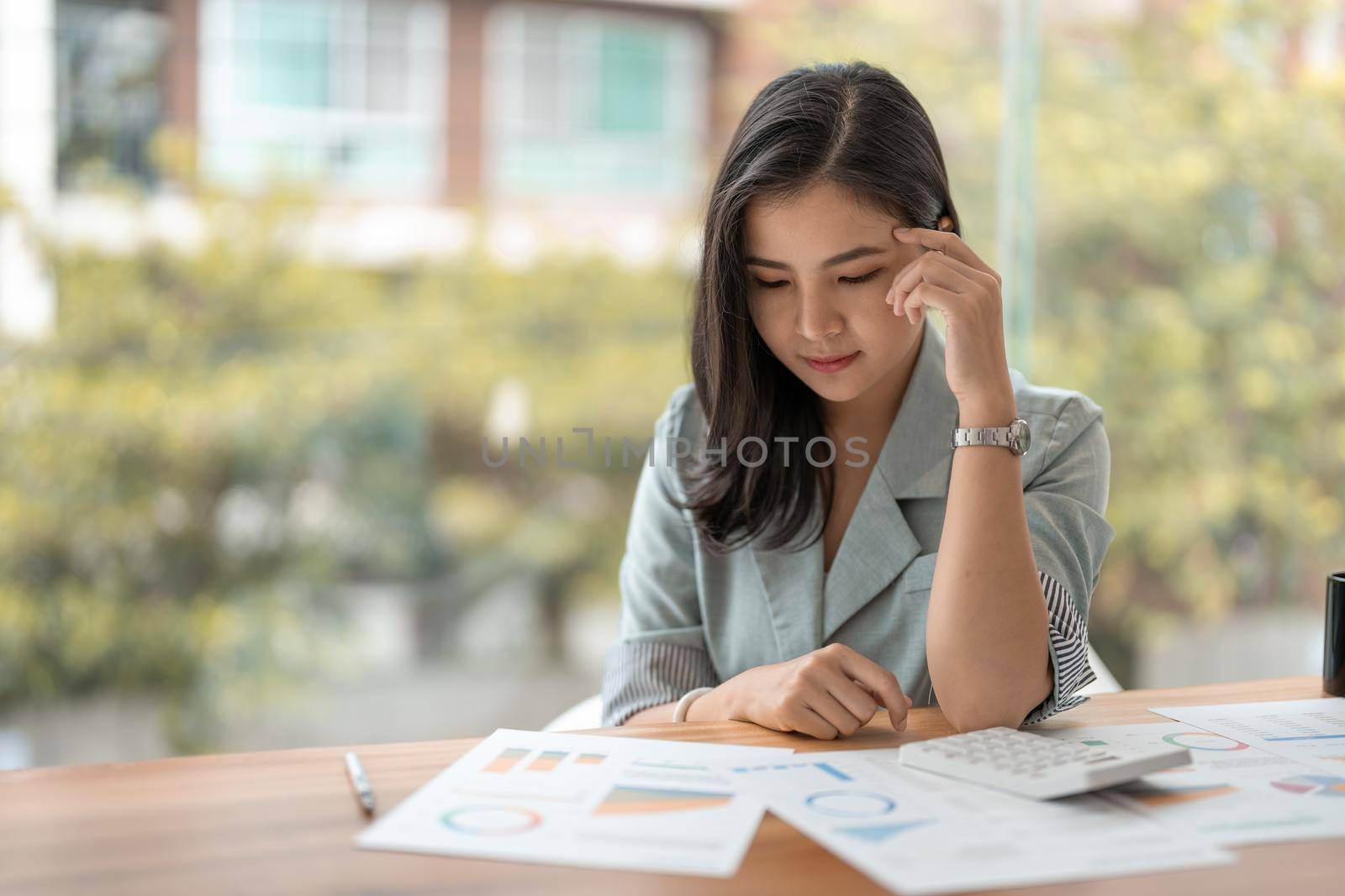 Thoughtful asian woman managing budget and finances using calculator in office, financial accounting concept