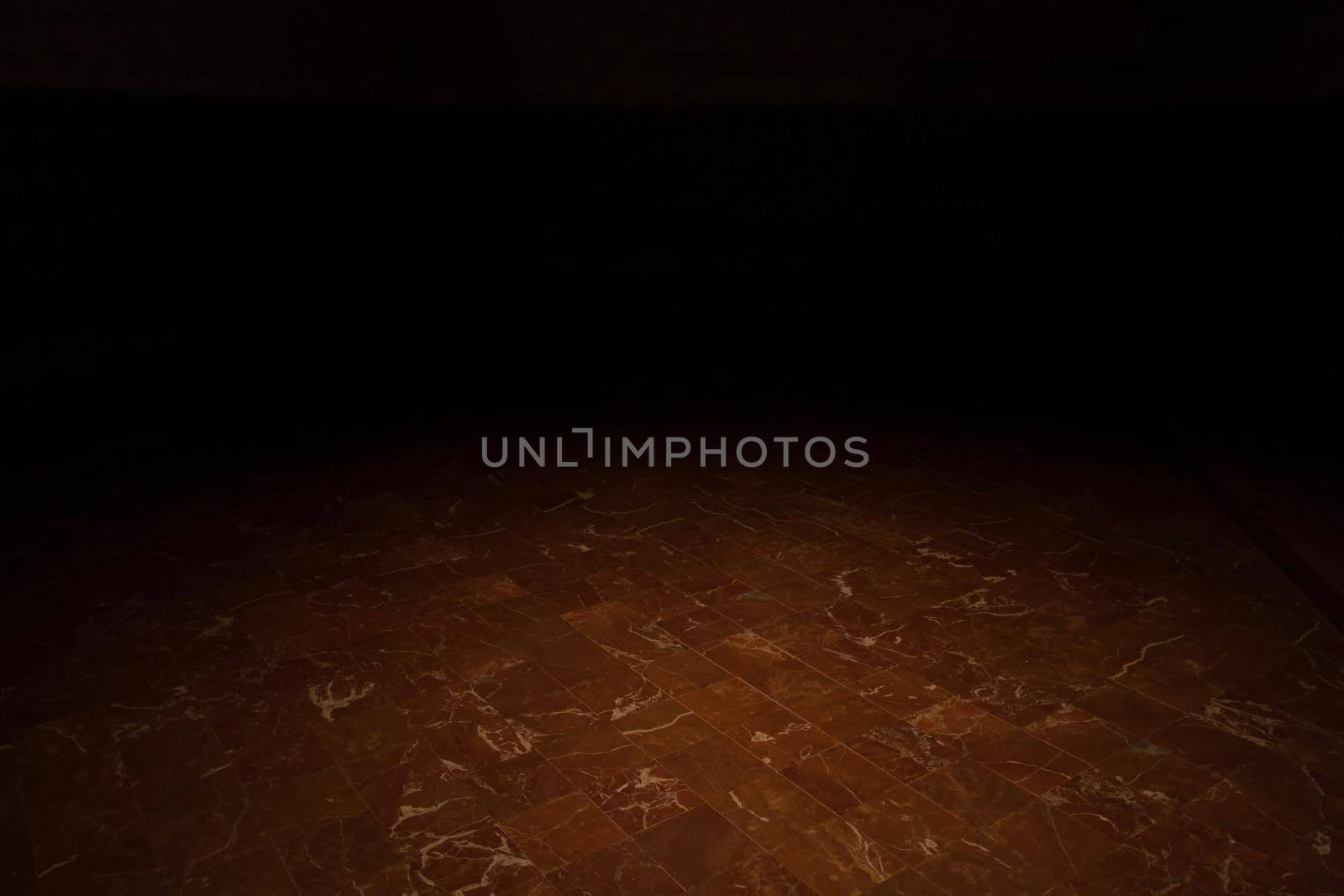 A very dark room with a spotlight on the red marble floor