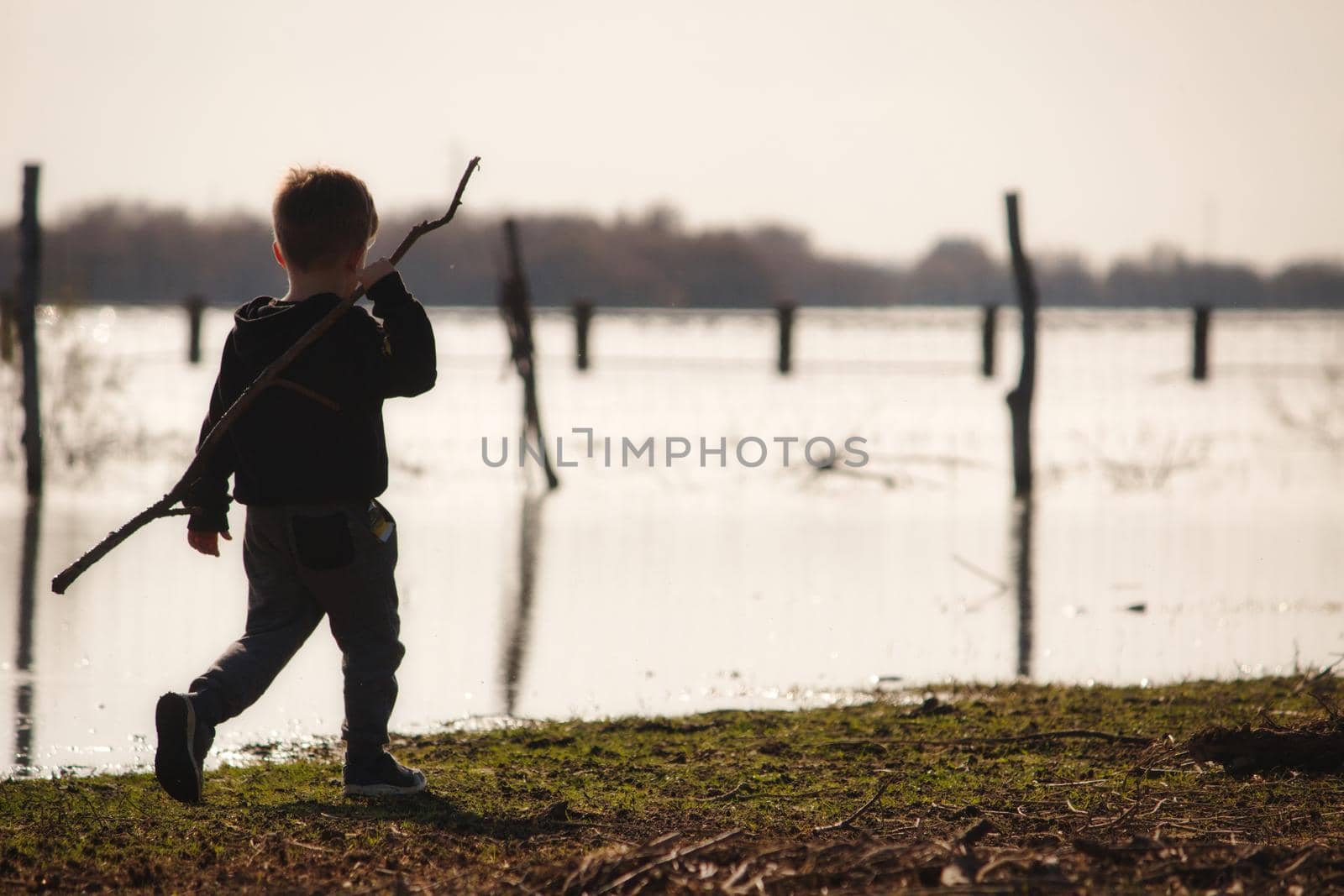 Young boy walking on the edge of a lake in winter holding a big stick