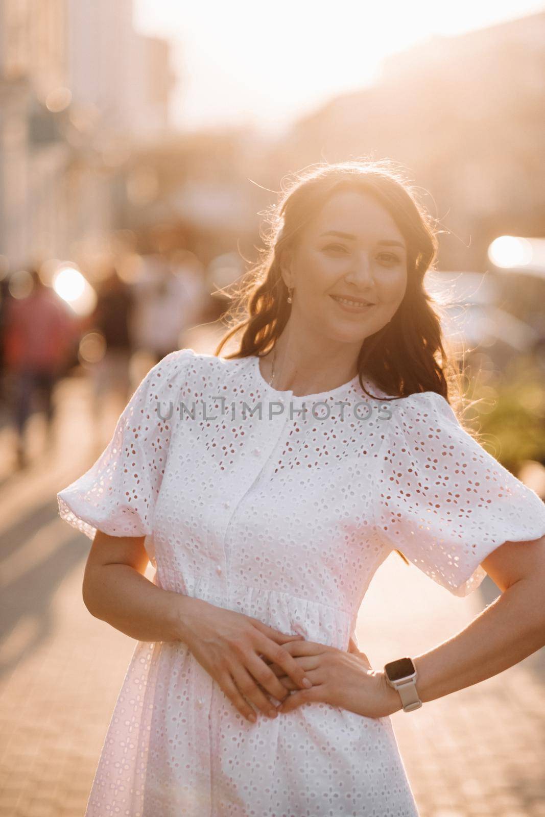 A beautiful woman in a white dress at sunset in the city. Evening street photography.