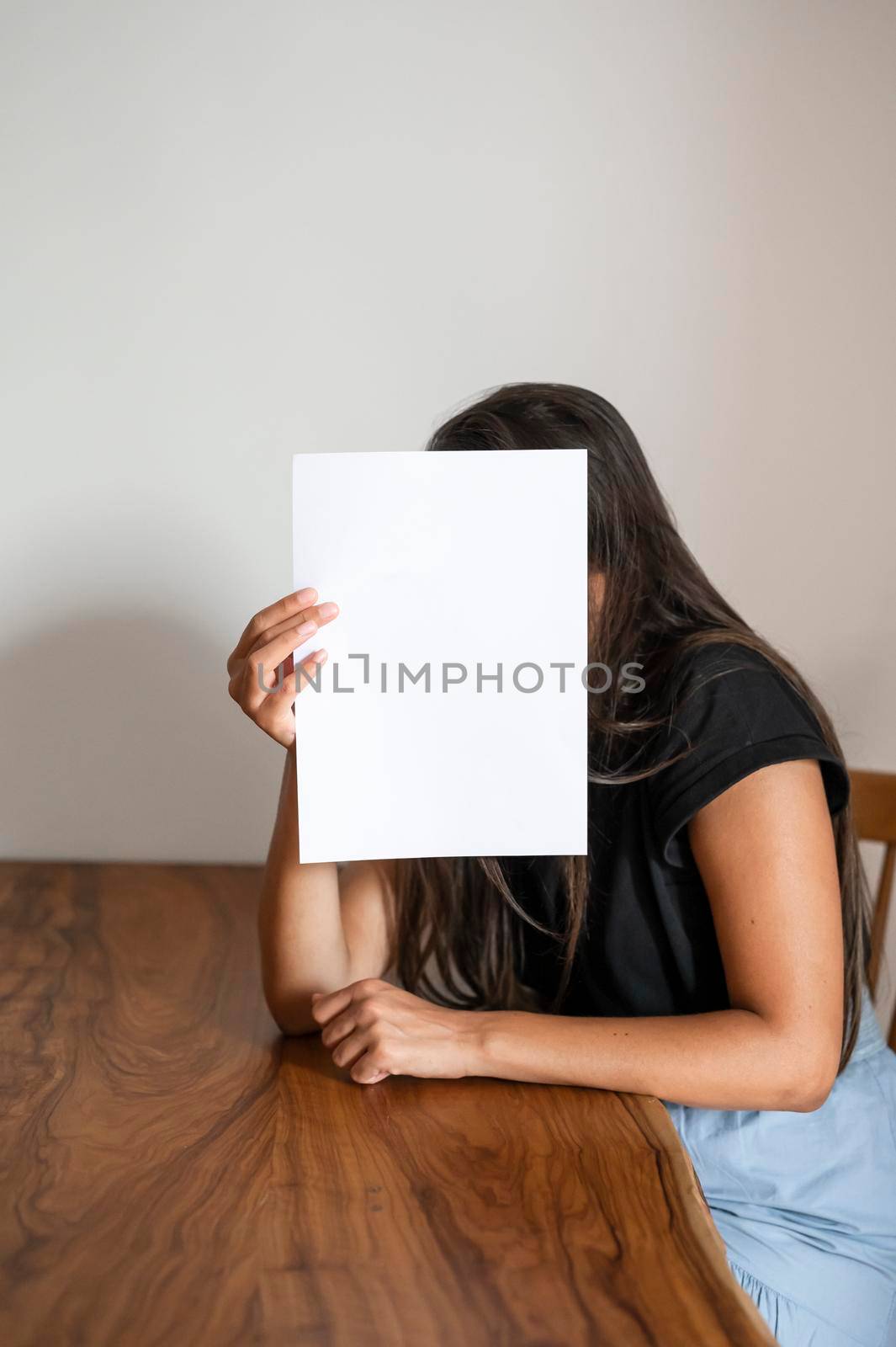 Woman hold a white paper sheet in front of her face.