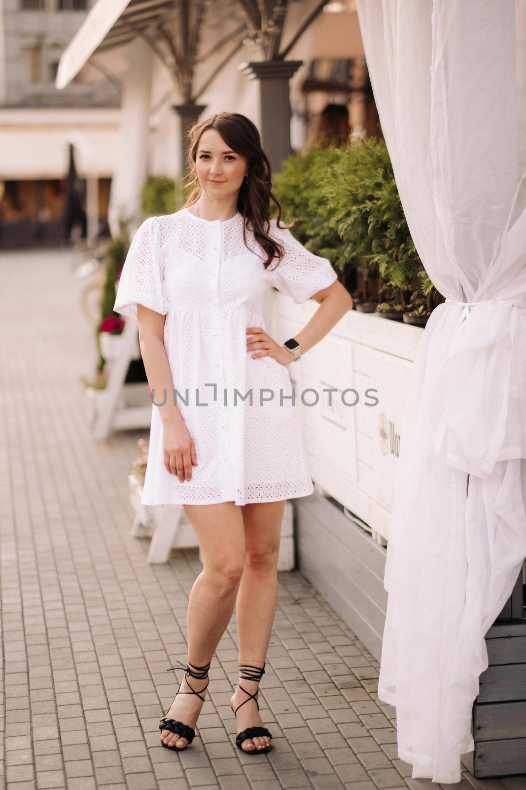 A beautiful woman in a white dress at sunset in the city. Evening street photography.