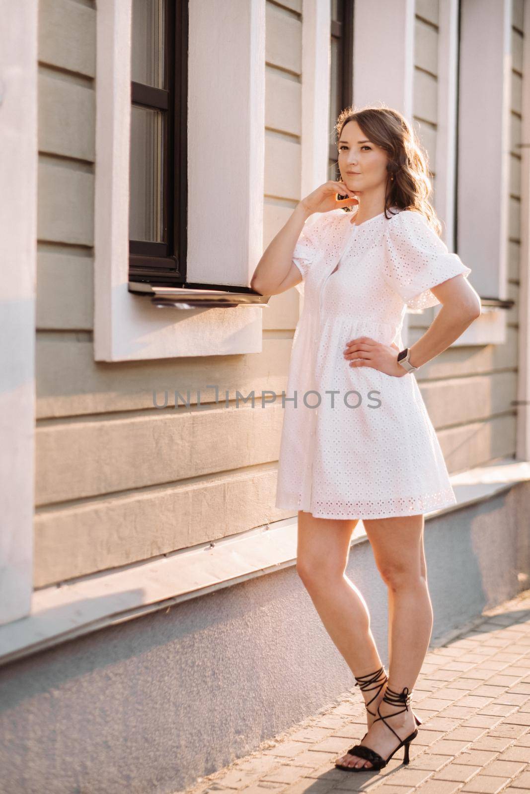 A beautiful woman in a white dress at sunset in the city. Evening street photography by Lobachad