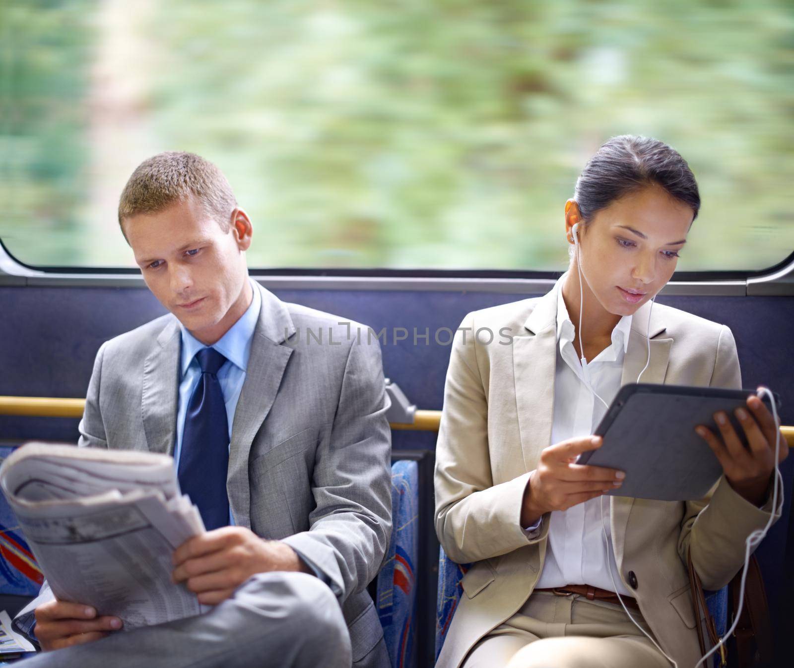 Optimizing their travel time wisely. Two business people reading catching up on the news on their commute to work. by YuriArcurs