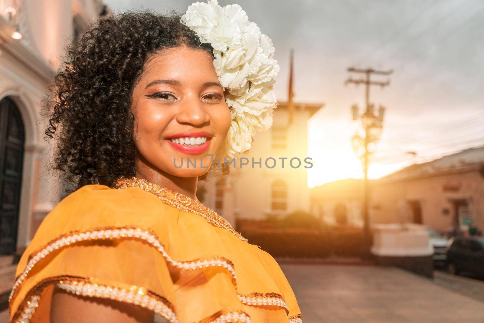 Mixed race teenager smiling wearing the classic Nicaraguan dress and flowers in her curly hair at sunset outside a colonial building