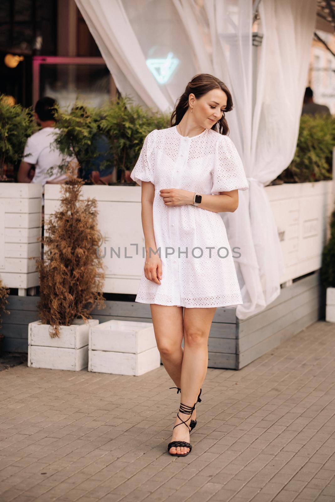 A beautiful woman in a white dress at sunset in the city. Evening street photography by Lobachad