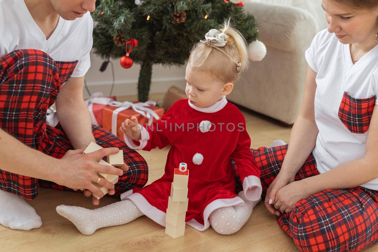 Toddler child with cochlear implant plays with parents under christmas tree - deafness and innovating medical technologies for hearing aid by Satura86