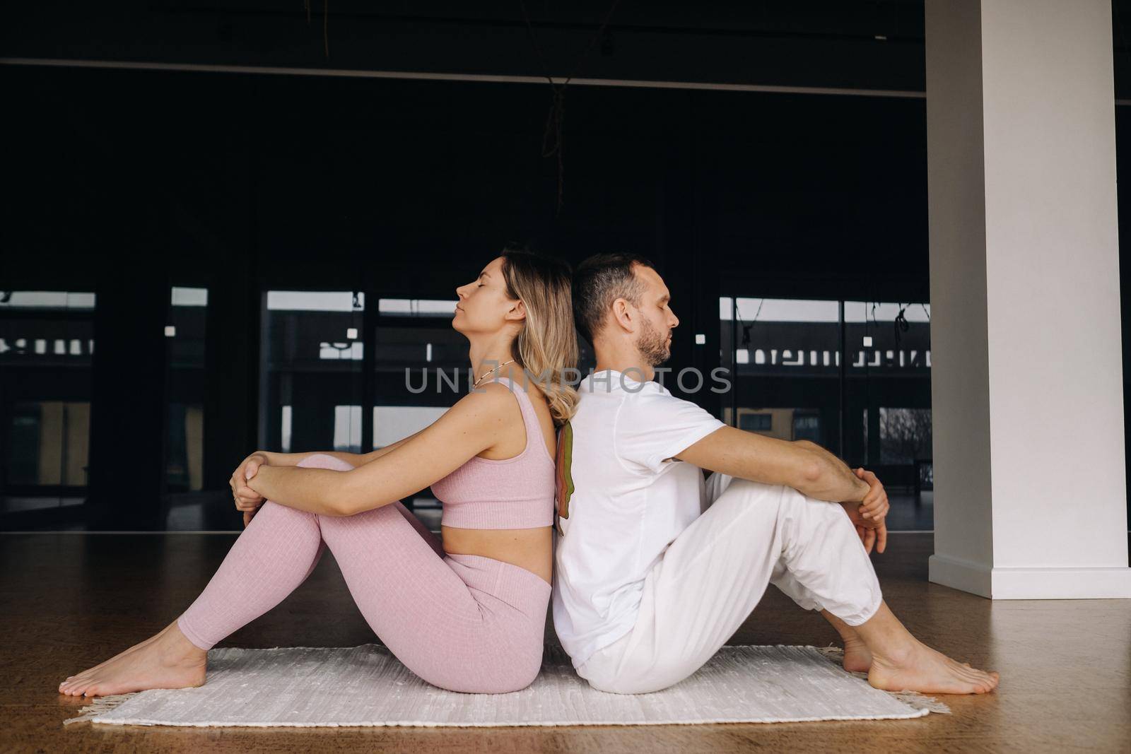 a woman and a man are engaged in pair gymnastics yoga in the gym by Lobachad