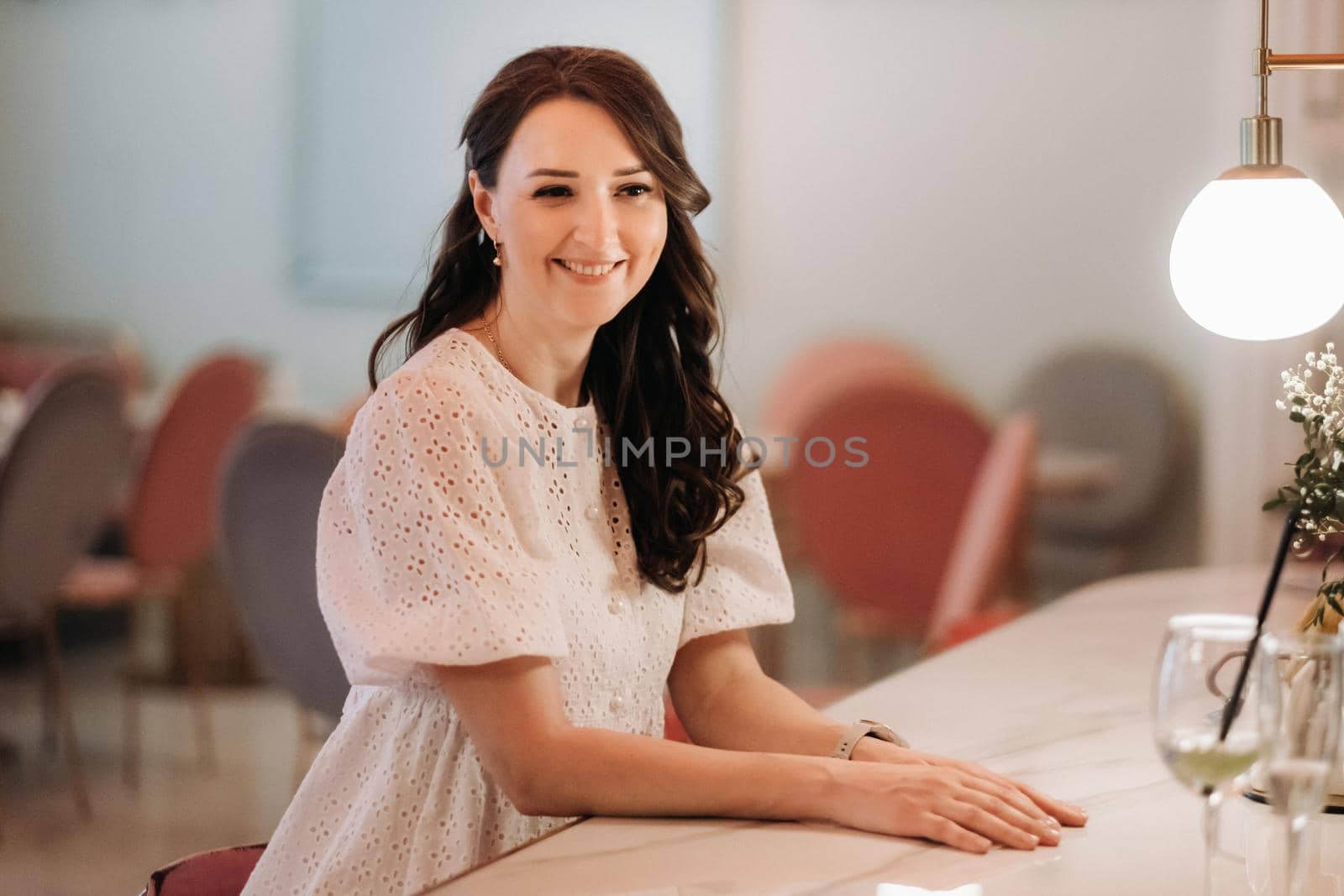 A girl in a white dress is sitting at the bar in a cafe and drinking a cocktail by Lobachad