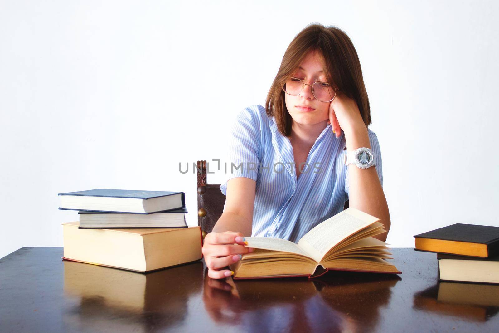 A white caucasian young teen student sitting at a table reading books looking bored