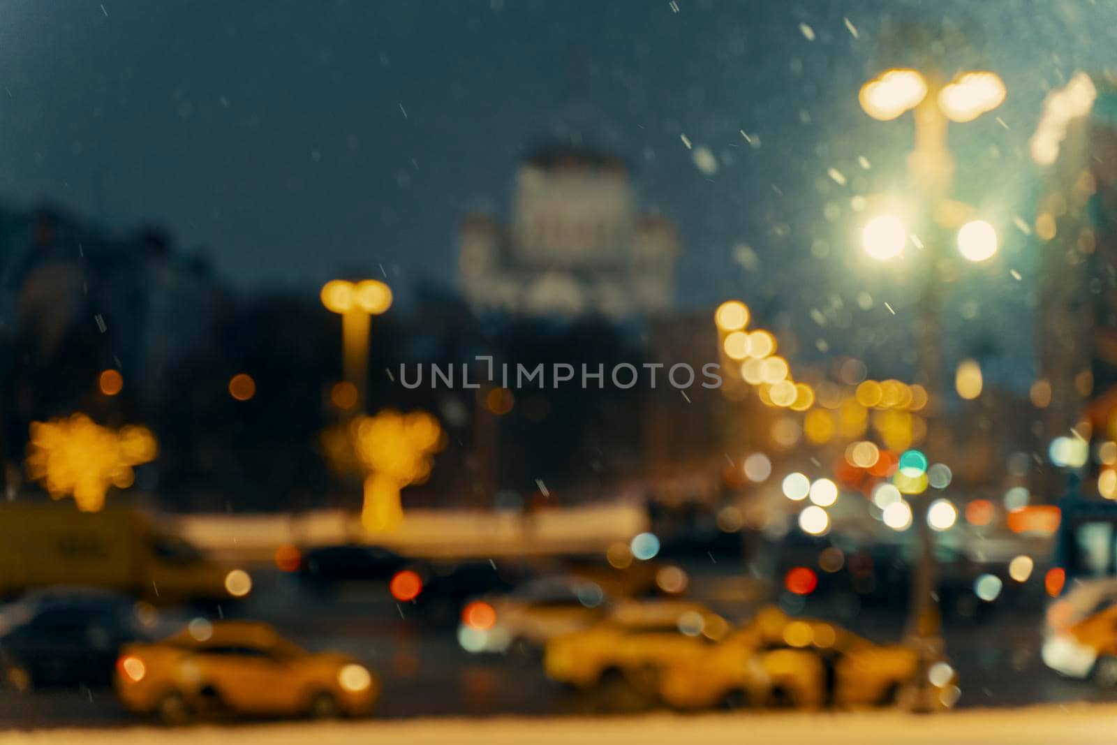 Winter blurred background with falling snow on the background of road traffic on a city street. Winter snowfall concept. Abstract bright bokeh.