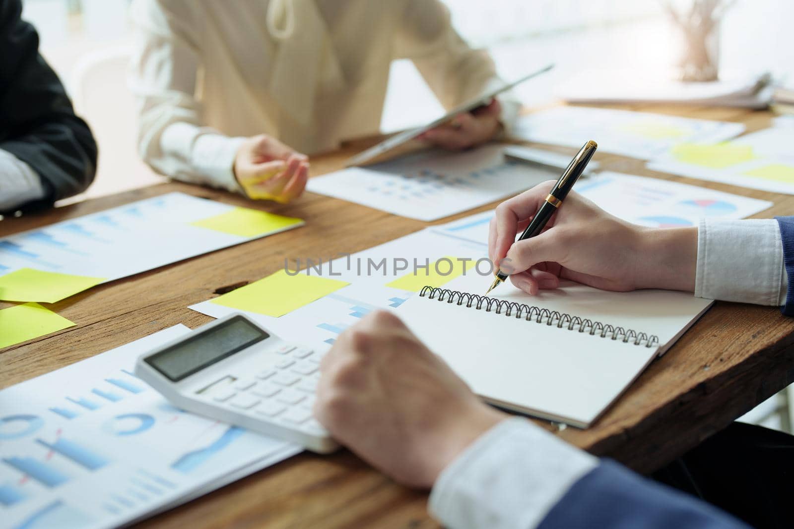 Male businessman holding pen to take notes summarizing marketing strategy with female colleagues in meeting, teamwork, investment planning by Manastrong