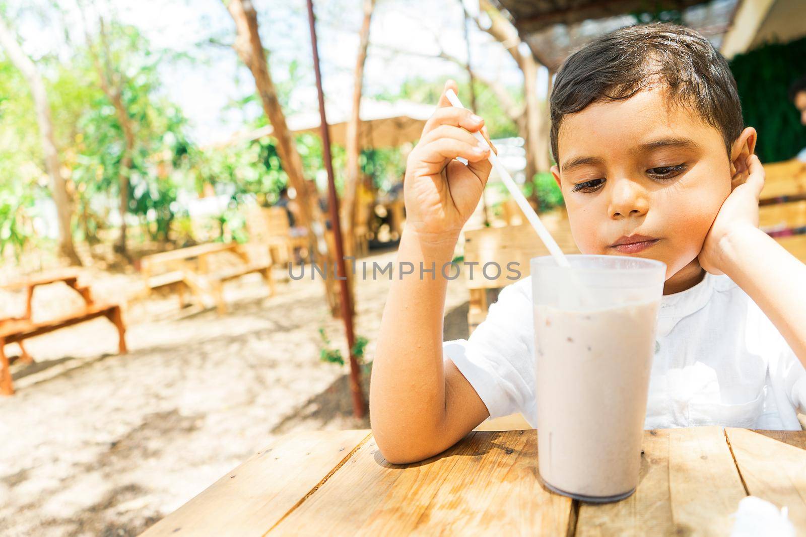 Latin boy drinking cocoa with milk in a restaurant in the countryside by cfalvarez