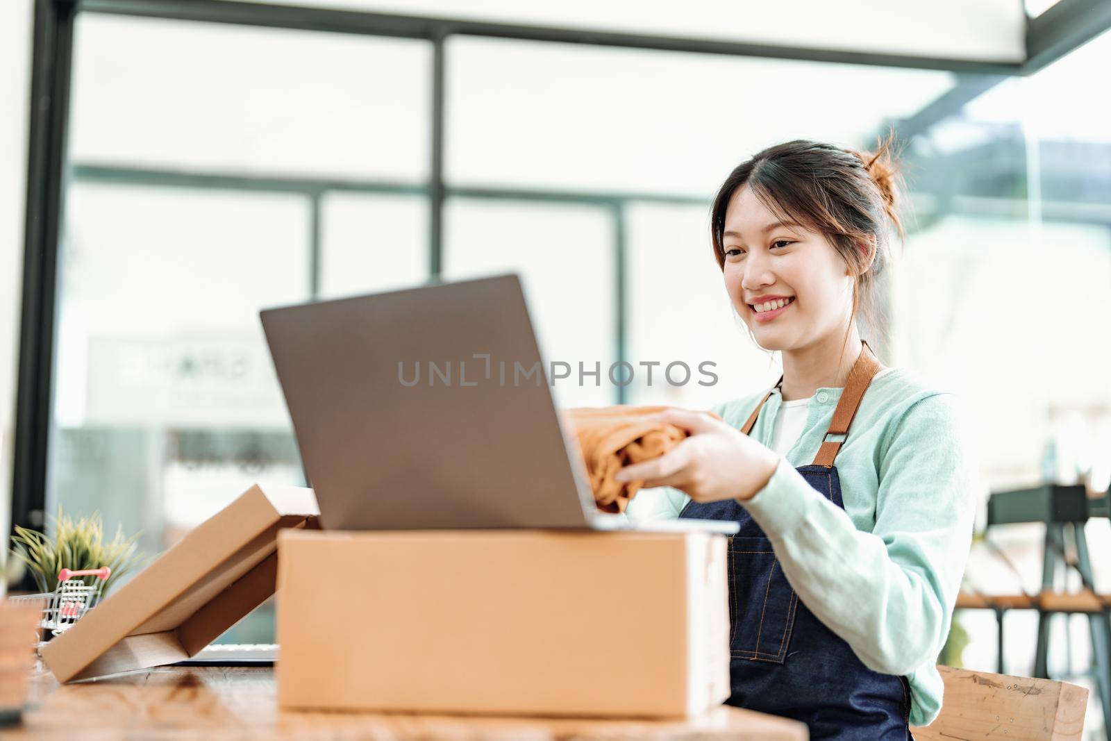 Portrait of a small startup business, SME owner, Asian female entrepreneur, talks to via video conferance, lets customers see products before pricing and packing them into boxes. Online Business by Manastrong