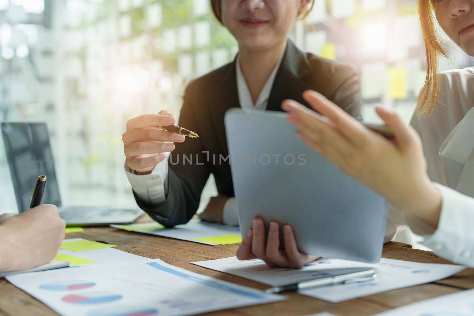 Businesswoman holding pen pointing at tablet to discuss marketing strategy summaries with colleagues in meetings, teamwork, investment planning by Manastrong