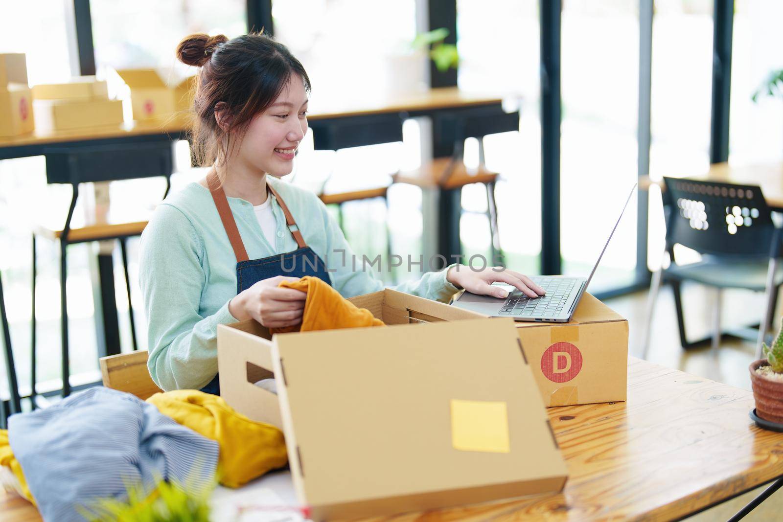 Portrait of a small startup business, SME owner, Asian female entrepreneur, talks to via video conferance, lets customers see products before pricing and packing them into boxes. Online Business by Manastrong