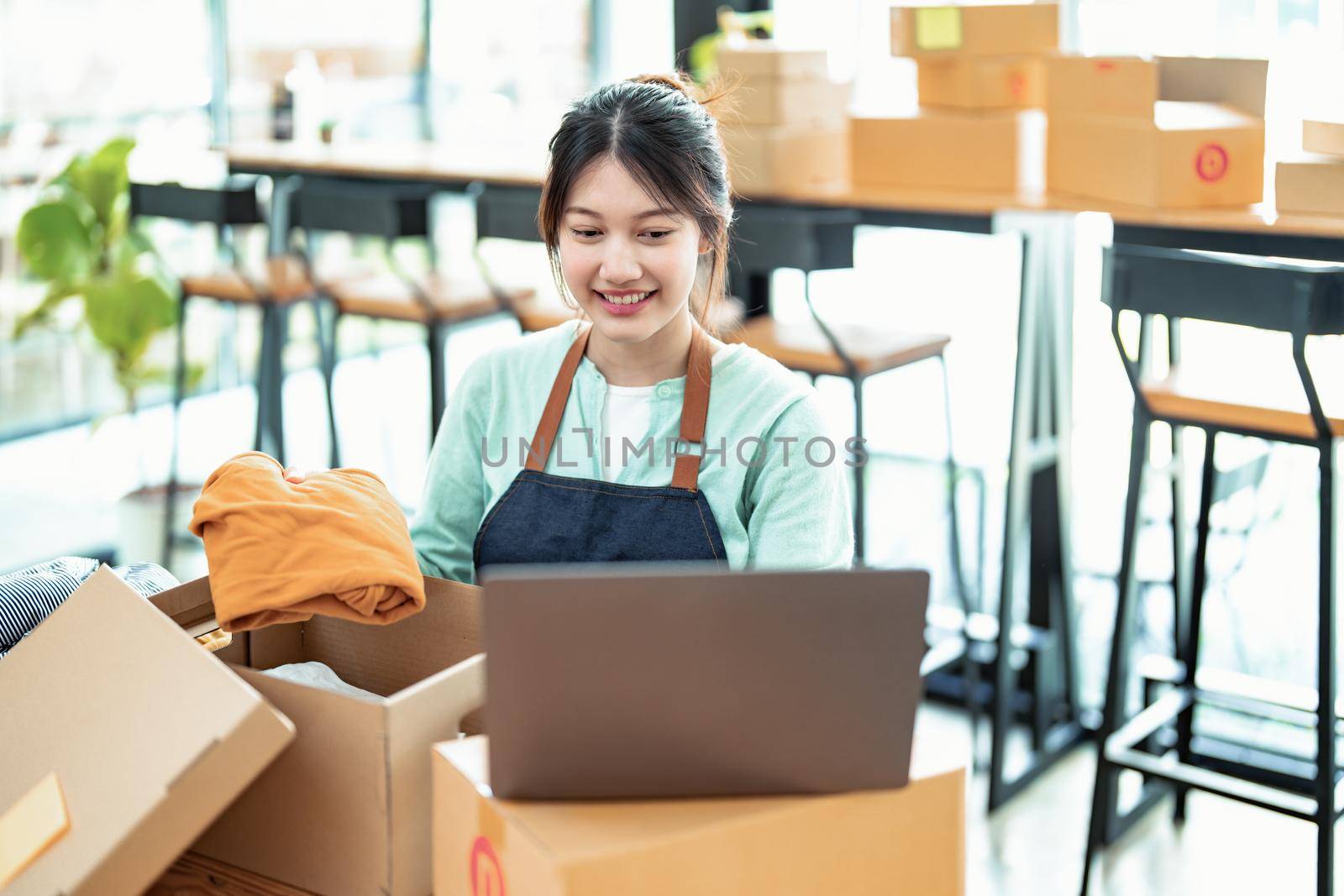 Portrait of a small startup business, SME owner, Asian female entrepreneur, talks to via video conferance, lets customers see products before pricing and packing them into boxes. Online Business by Manastrong