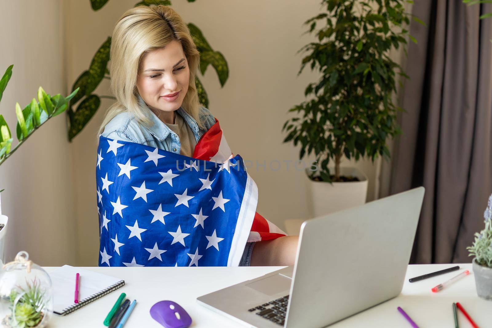 Happy young female student hold flag of USA, studying with laptop with blank screen in living room interior. International education at home, lesson remote, website due covid-19 quarantine by Andelov13