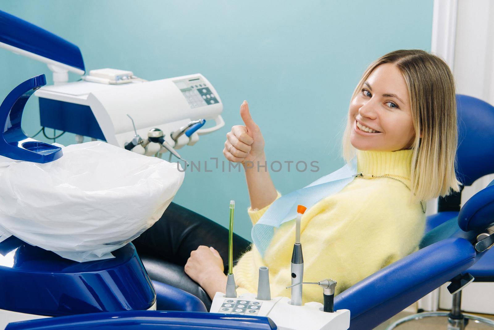 Beautiful girl patient shows the class with her hand while sitting in the Dentist's chair.