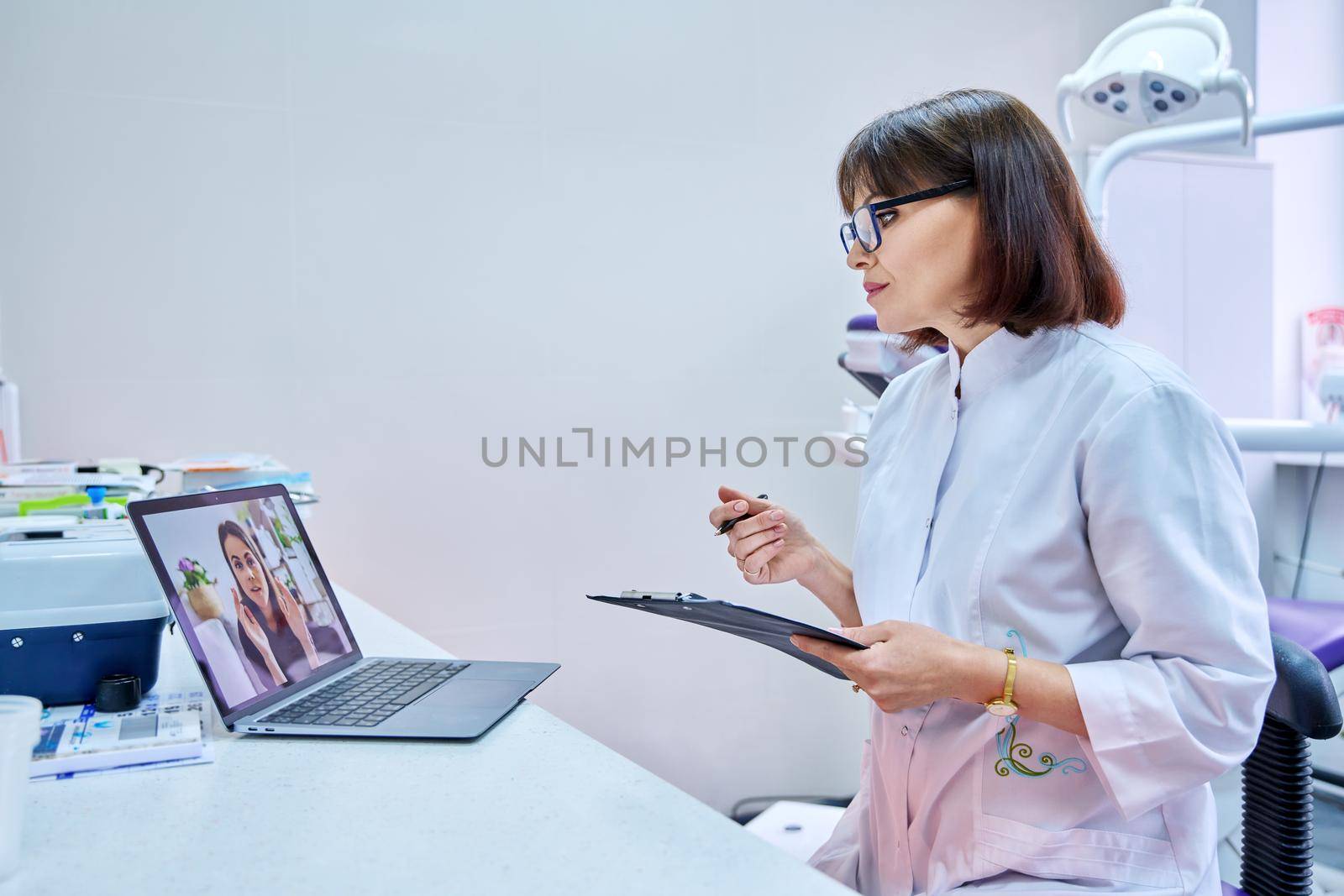 Video chat call conference of doctor dentist and young woman patient on laptop screen, in dental office. Online meeting, consultation, service, dentistry, medicine, technology concept
