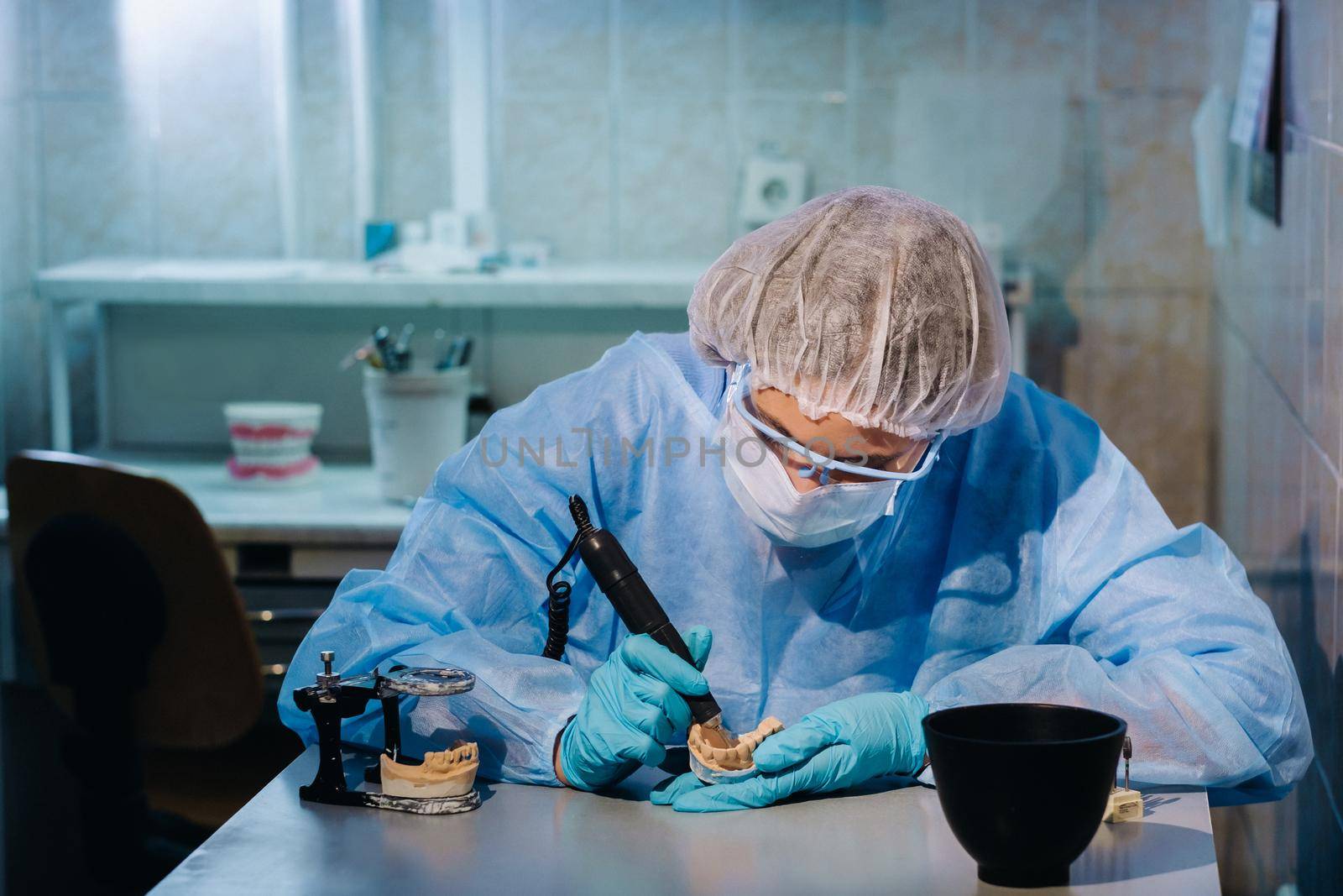 A dental technician in protective clothing is working on a prosthetic tooth in his laboratory.