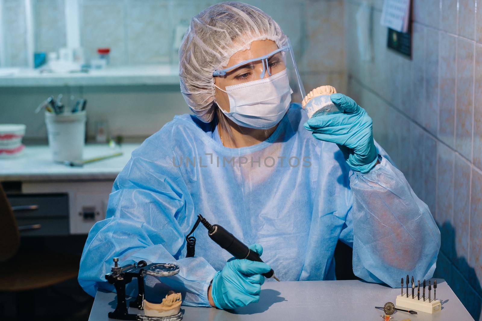 A dental technician in protective clothing is working on a prosthetic tooth in his laboratory.