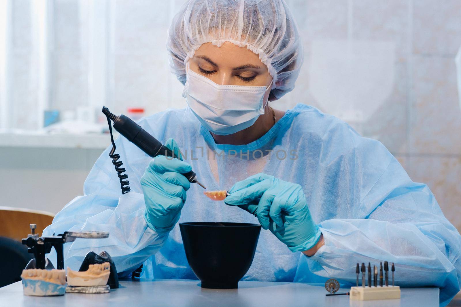 A dental technician in protective clothing is working on a prosthetic tooth in his laboratory by Lobachad