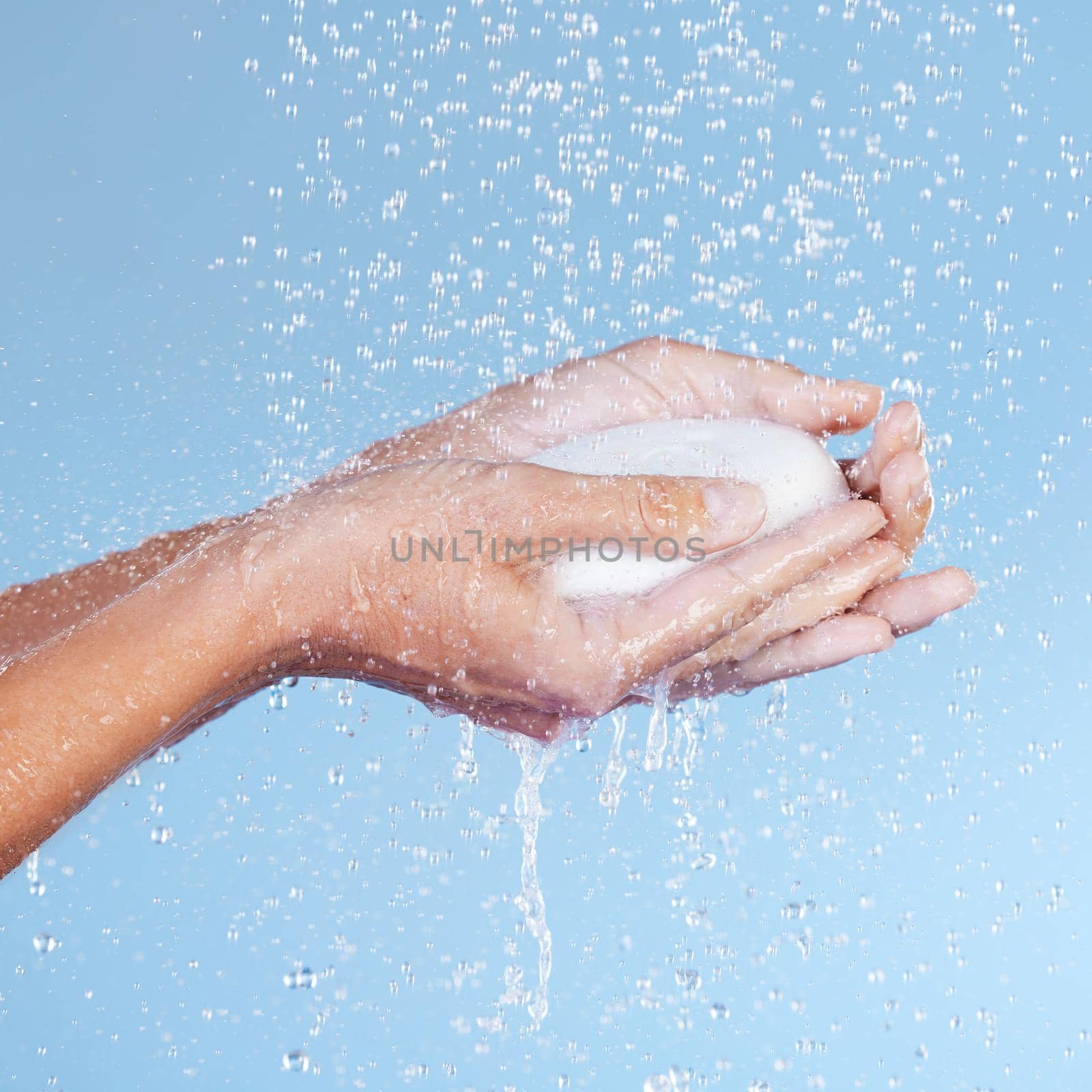 Water and soap are your best friends. Studio shot of an unrecognisable woman holding a bar of soap while taking a shower against a blue background. by YuriArcurs