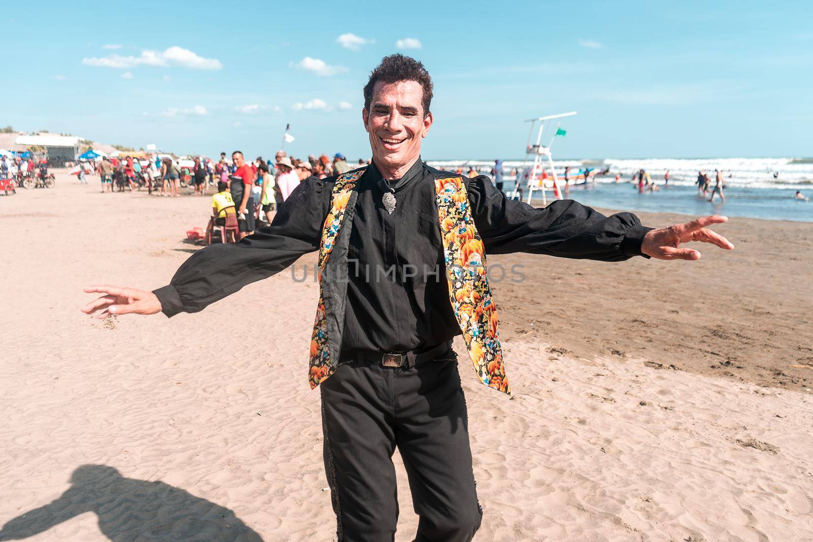 Portrait of a Latin man dressed in black and with a flowered vest dancing with open arms and looking at the camera. Concept of celebration of summer break in Latin America.