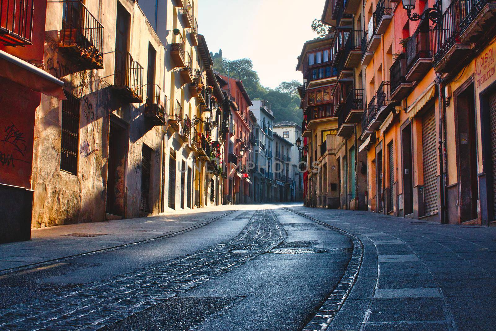 A moody and picturesque view of a street in Granada, Spain, winding uphill with tall buildings on either side by tennesseewitney