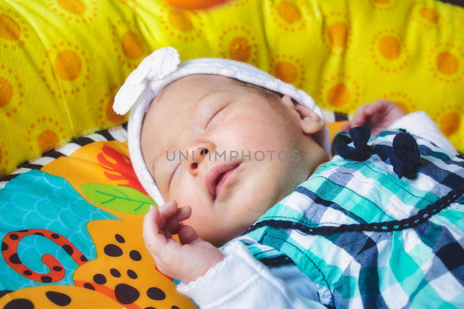 An adorable cute newborn baby girl wearing a white headband fast asleep on a play blanket