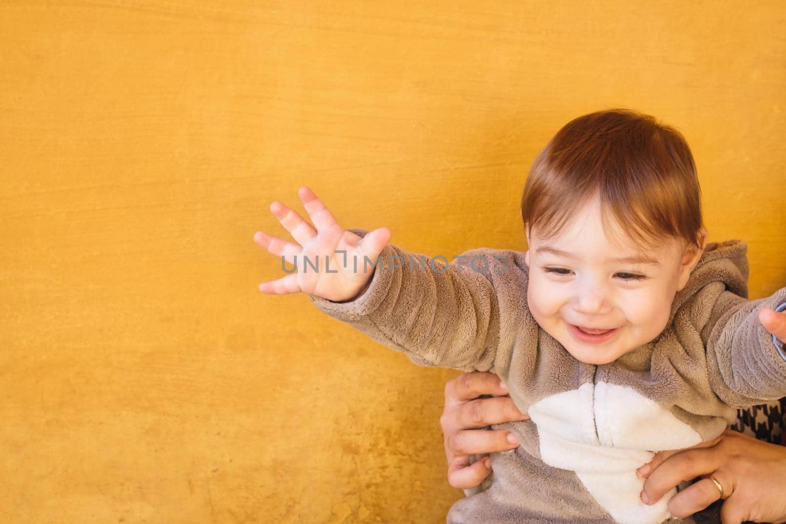 Adorable baby toddler boy wearing a warm winter onesie jumpsuit against a bright orange wall background