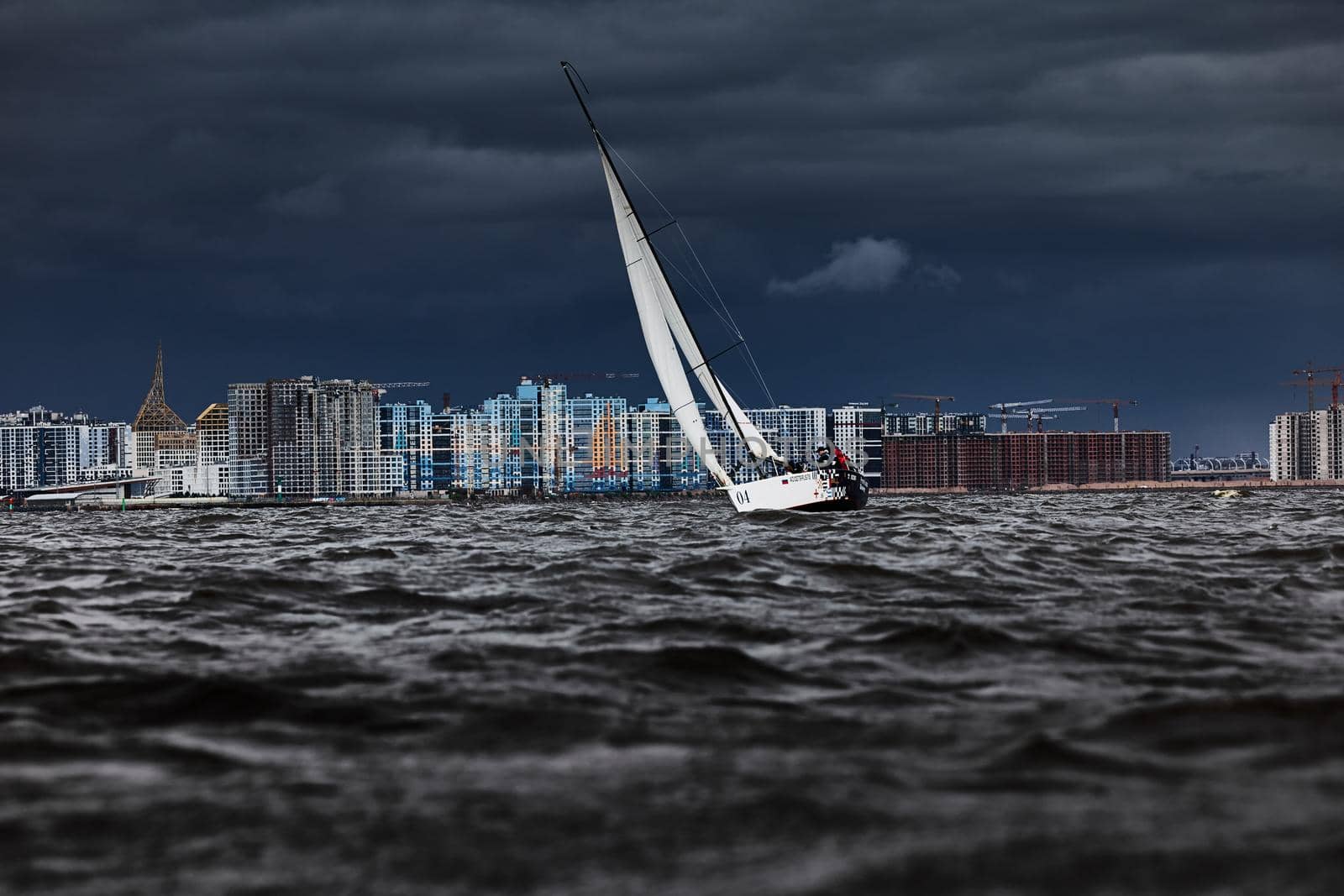 Russia, St. Petersburg, 17 June 2022: The residential complex under construction on the embankment of the Neva River on Vasilievsky island in stormy weather, construction cranes, sailing yachts. High quality photo