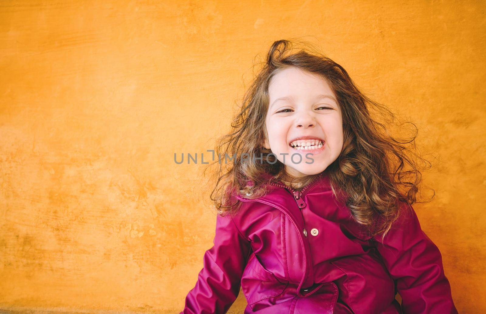 Young girl with a cheeky smile looking directly at the camera against a bright yellow wall background by tennesseewitney