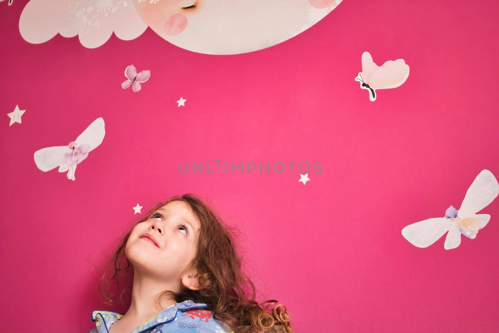 Young cute girl wearing pajamas looking up at a pink wall with decal stars, moon and fairies by tennesseewitney