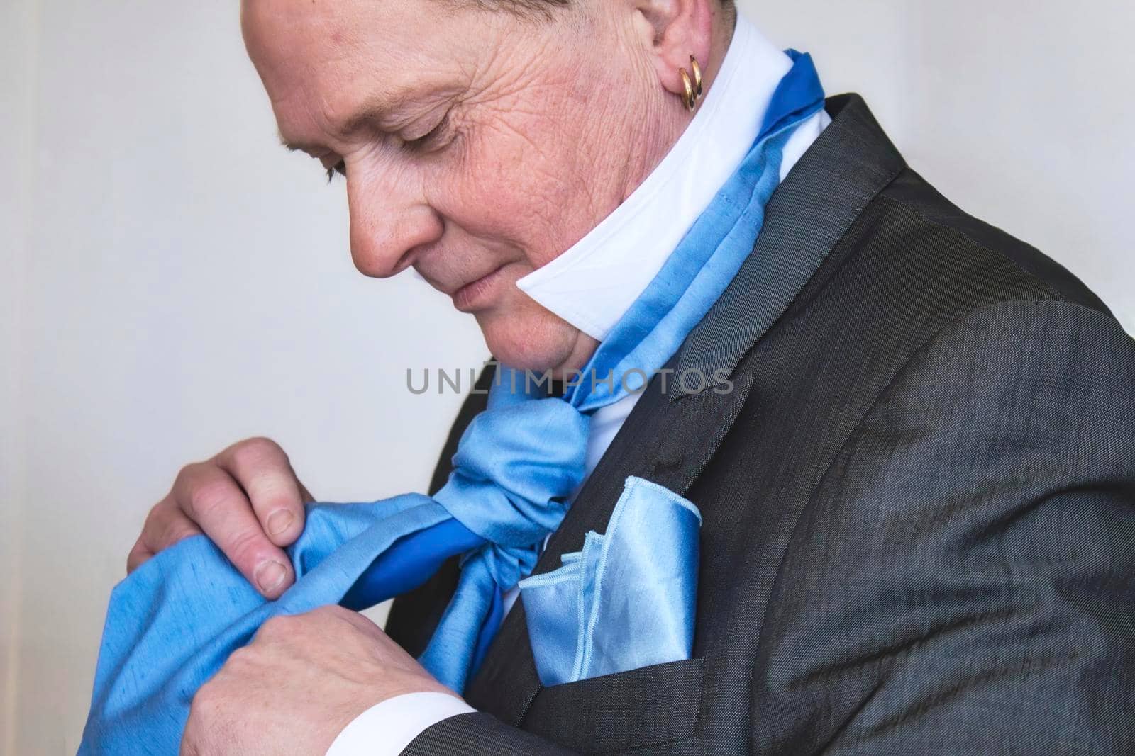 A middle-aged man putting on a silk blue tie dressed in a suit getting ready for a wedding by tennesseewitney