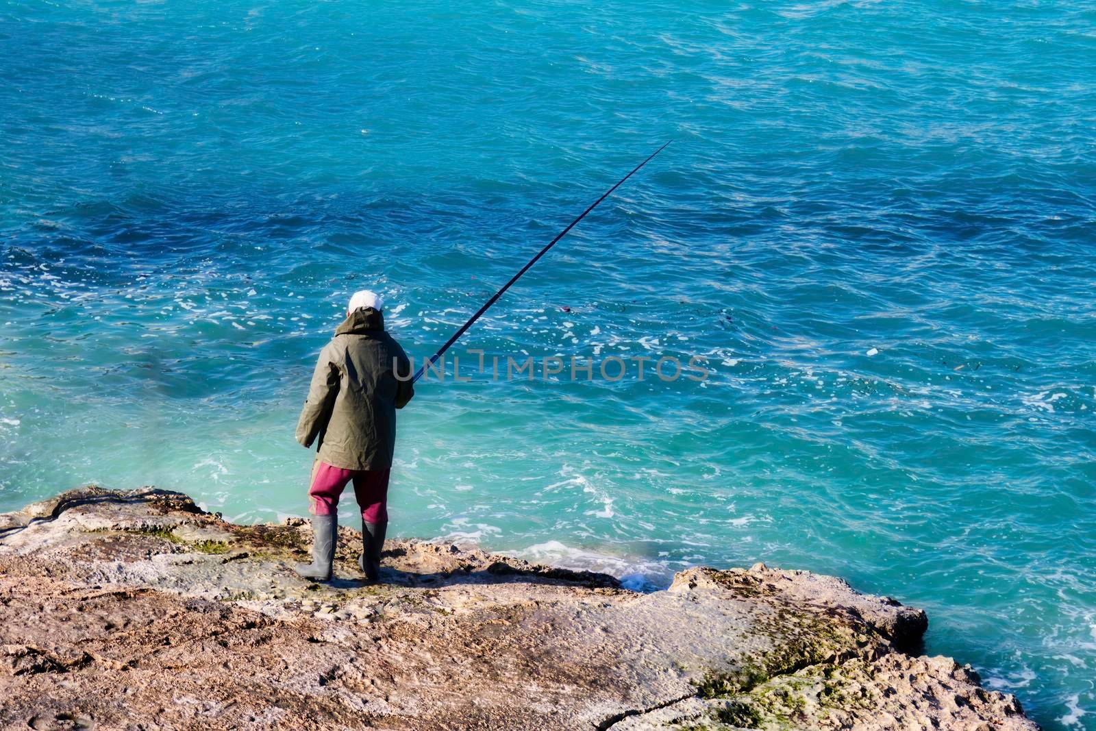 Fisherman stood on a rocky beach fishing with a rod in winter