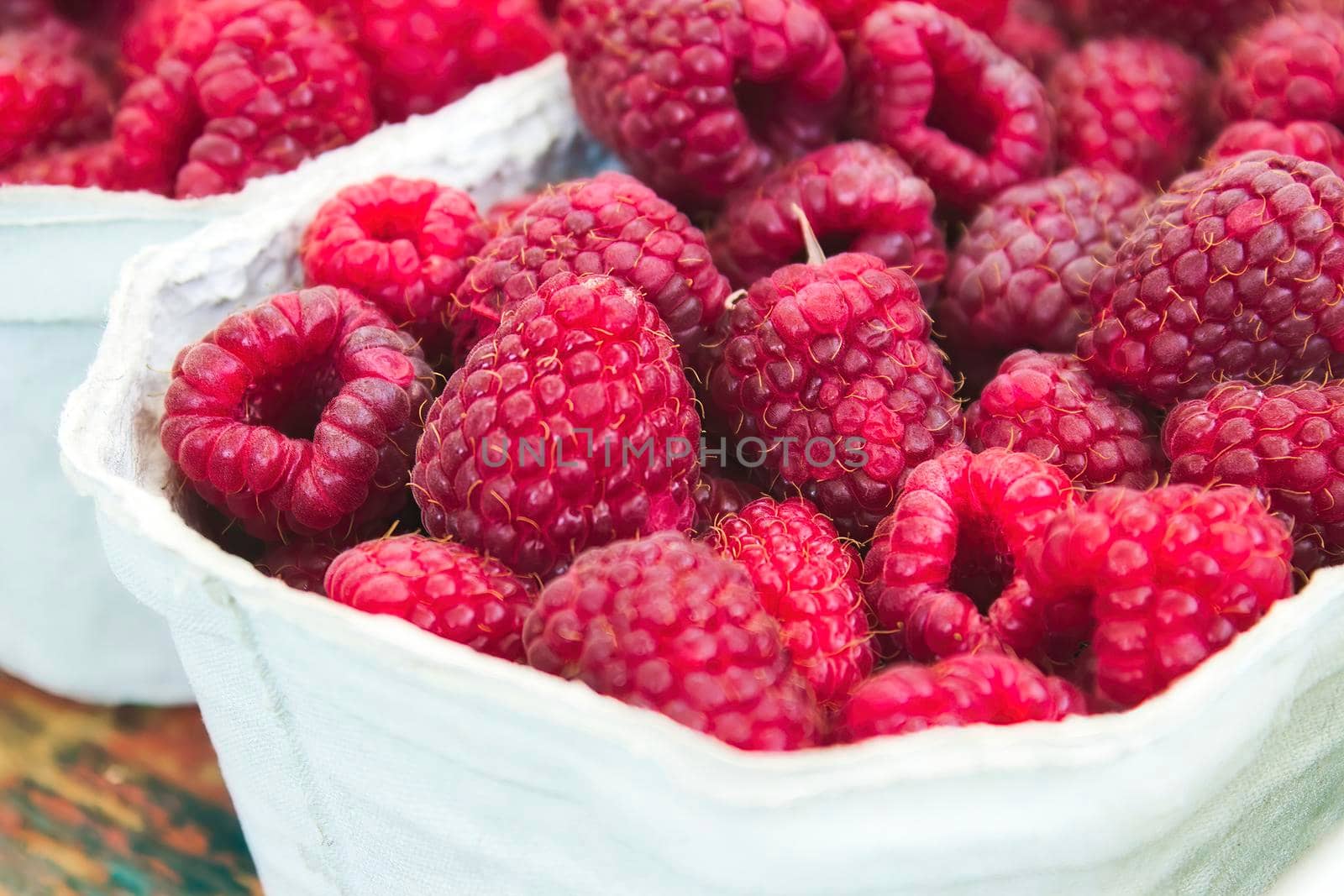 Close-up of a container of fresh, red, ripe raspberries at an open-air food market