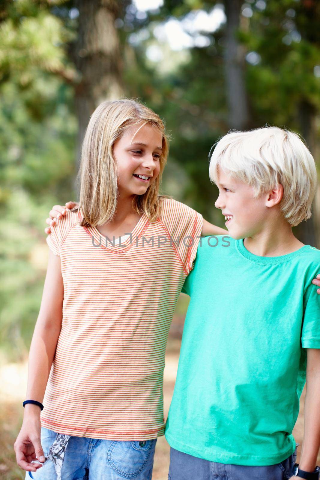 Young siblings standing outdoors with arms around.